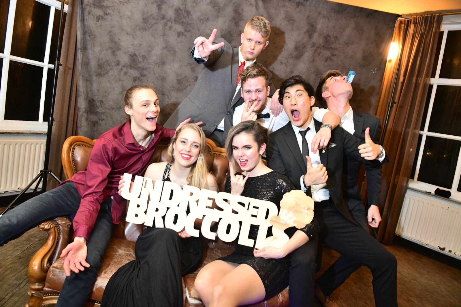 Undressed Broccoli piled onto a leather couch at a student gala, holding the band's wooden nameplate.